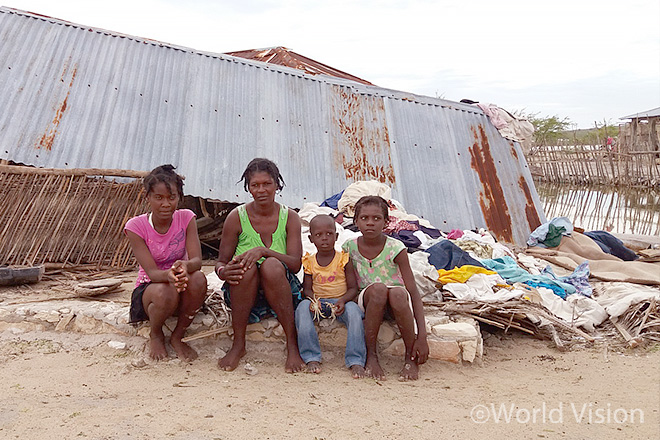허리케인으로 무너진 집 앞에 주저앉아 있는 아이본과 그녀의 가족들(사진출처: 월드비전)